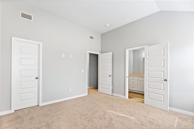 unfurnished bedroom featuring light colored carpet, lofted ceiling, and connected bathroom