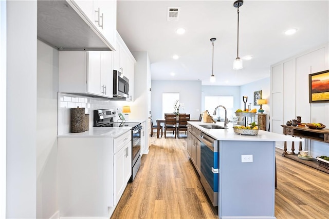 kitchen featuring pendant lighting, a kitchen island with sink, white cabinets, sink, and appliances with stainless steel finishes