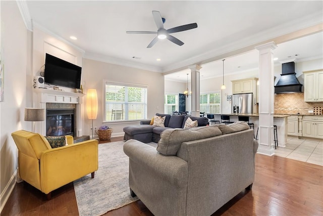 living area featuring ceiling fan, ornate columns, a glass covered fireplace, recessed lighting, and light wood-style flooring