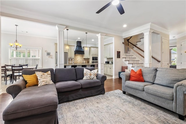 living area featuring crown molding, decorative columns, a wealth of natural light, and ceiling fan with notable chandelier