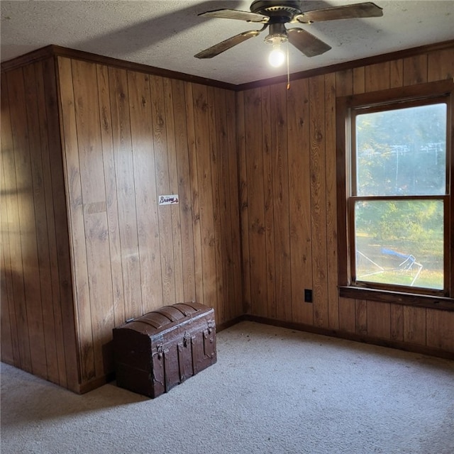 empty room featuring a textured ceiling, light colored carpet, ceiling fan, and wood walls