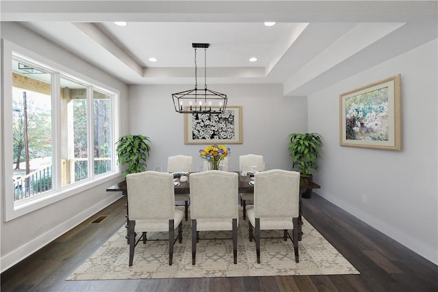 dining space featuring dark wood-type flooring, a tray ceiling, and a notable chandelier