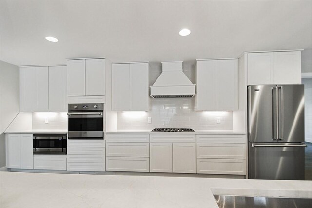 kitchen featuring premium range hood, backsplash, white cabinets, and appliances with stainless steel finishes