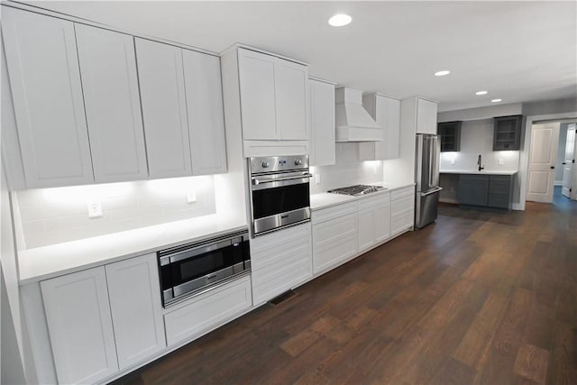 kitchen with white cabinetry, dark hardwood / wood-style flooring, custom range hood, and appliances with stainless steel finishes