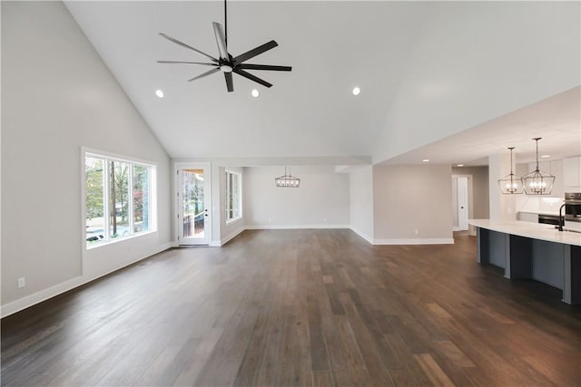 unfurnished living room with ceiling fan with notable chandelier, dark hardwood / wood-style floors, and high vaulted ceiling