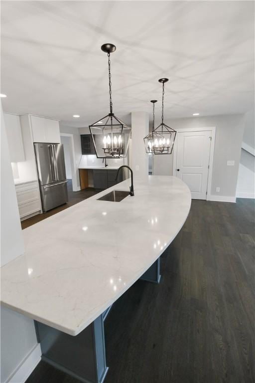 kitchen featuring a breakfast bar, sink, pendant lighting, white cabinetry, and stainless steel refrigerator