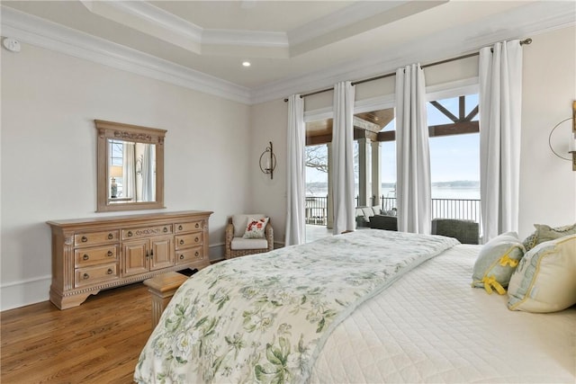 bedroom with a tray ceiling, hardwood / wood-style floors, crown molding, and access to outside