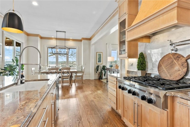 kitchen with light brown cabinetry, hanging light fixtures, custom range hood, stainless steel gas stovetop, and light hardwood / wood-style floors