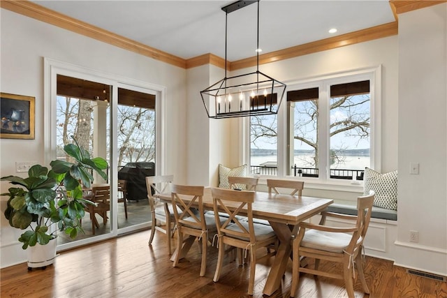 dining area with a water view, crown molding, a chandelier, and hardwood / wood-style floors