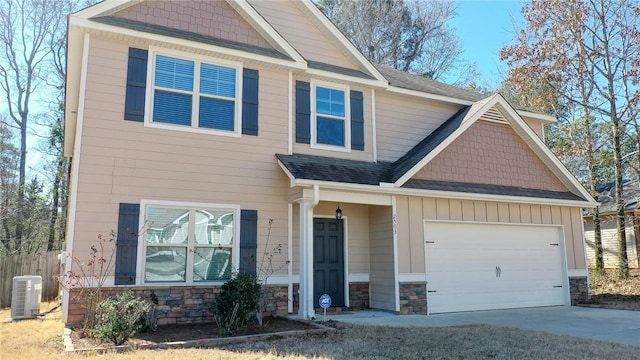 craftsman inspired home with driveway, stone siding, an attached garage, fence, and central AC