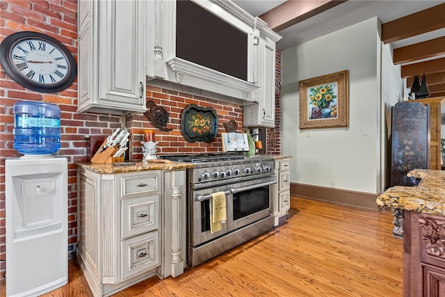 kitchen featuring white cabinets, light hardwood / wood-style floors, range with two ovens, and brick wall