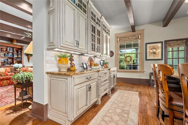 bar with ceiling fan, light stone countertops, beamed ceiling, backsplash, and light wood-type flooring