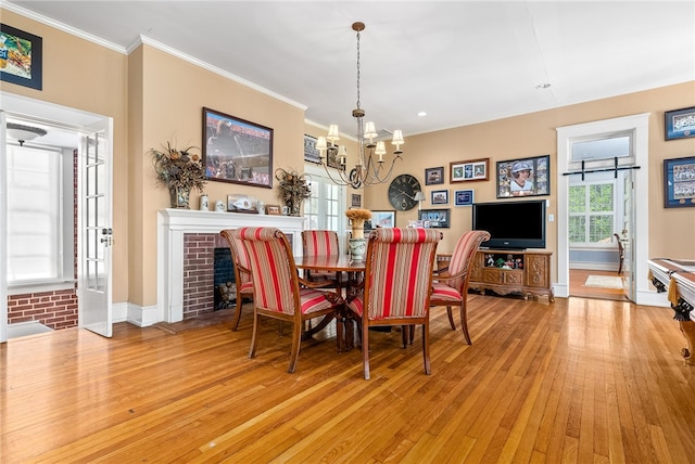 dining room with a brick fireplace, light hardwood / wood-style flooring, a notable chandelier, and crown molding