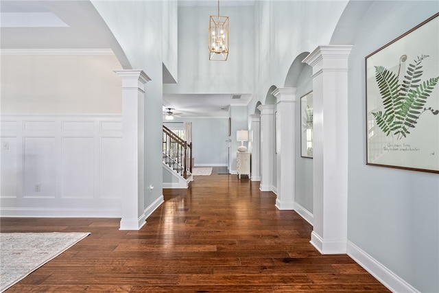 foyer featuring dark wood-style floors, arched walkways, decorative columns, stairway, and ceiling fan with notable chandelier