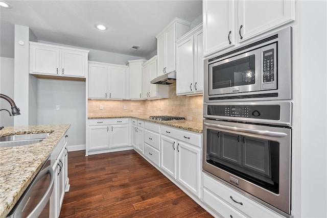 kitchen with decorative backsplash, stainless steel appliances, under cabinet range hood, white cabinetry, and a sink