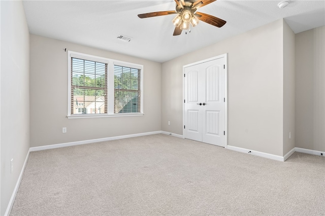 spare room with light carpet, ceiling fan, visible vents, and baseboards