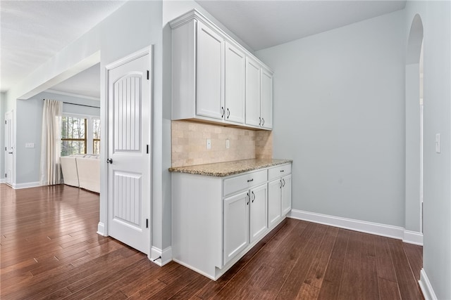 kitchen featuring dark wood-style floors, white cabinetry, arched walkways, and backsplash