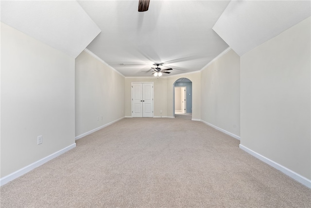 unfurnished room featuring arched walkways, baseboards, light colored carpet, ceiling fan, and ornamental molding