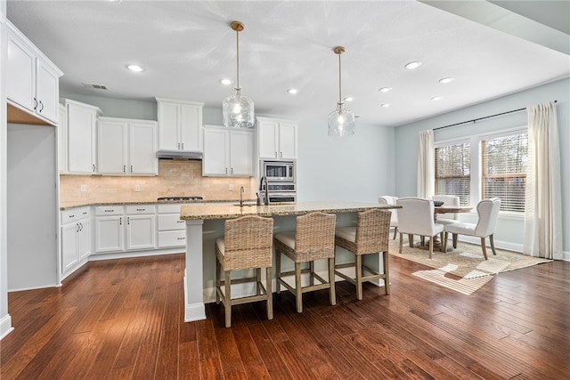 kitchen with under cabinet range hood, visible vents, stainless steel appliances, and dark wood-type flooring