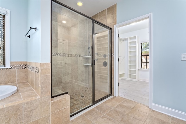 bathroom with a walk in closet, a garden tub, a stall shower, baseboards, and tile patterned floors