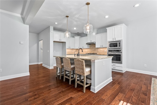 kitchen featuring under cabinet range hood, baseboards, appliances with stainless steel finishes, dark wood-style floors, and tasteful backsplash