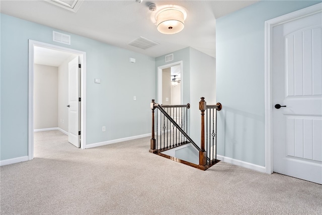 hallway featuring carpet floors, baseboards, visible vents, and an upstairs landing