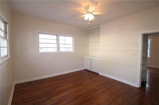 spare room with dark hardwood / wood-style flooring, built in shelves, a wealth of natural light, and ornamental molding