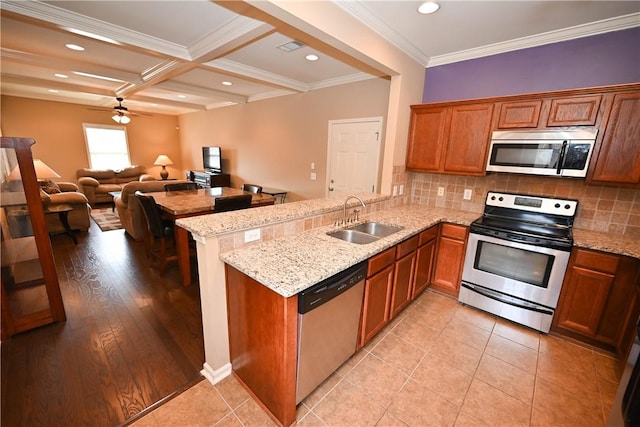 kitchen with sink, stainless steel appliances, light stone counters, decorative backsplash, and kitchen peninsula