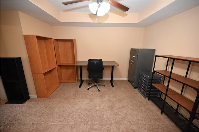 office featuring a raised ceiling, light carpet, and ceiling fan