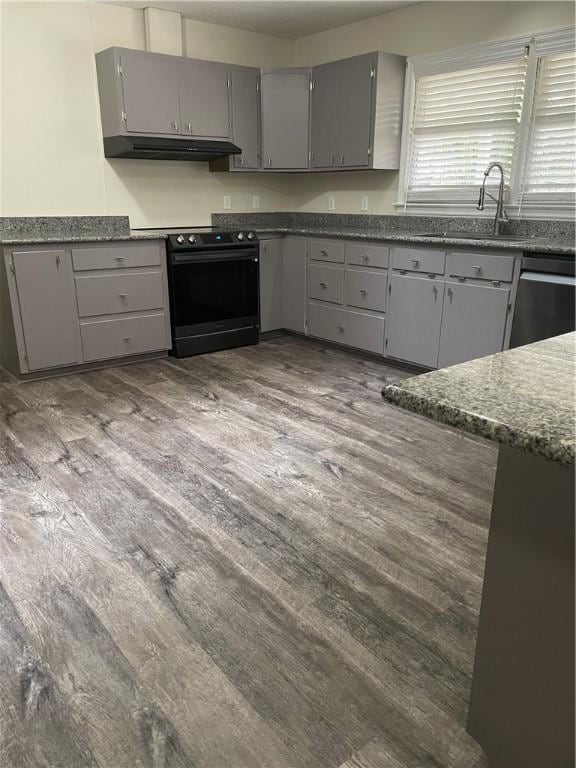 kitchen with dark stone counters, black appliances, gray cabinetry, and light hardwood / wood-style flooring