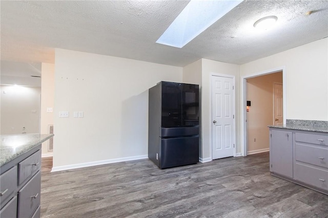 kitchen with black fridge, hardwood / wood-style floors, a textured ceiling, and a skylight