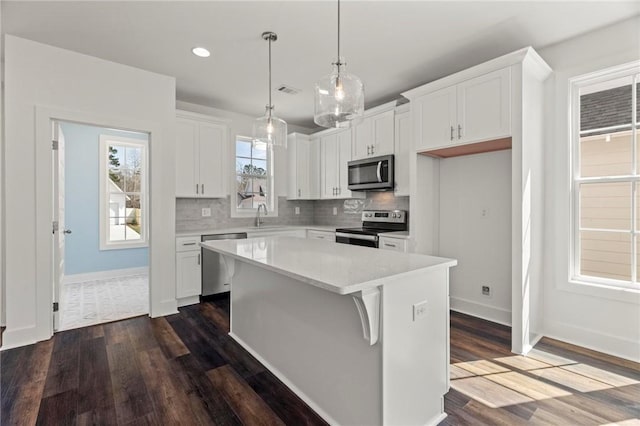 kitchen featuring a kitchen island, white cabinetry, light countertops, appliances with stainless steel finishes, and backsplash