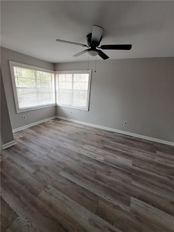 empty room with a ceiling fan, dark wood finished floors, and baseboards