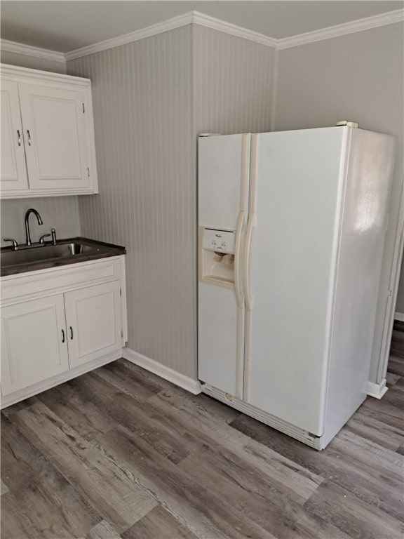 kitchen featuring dark countertops, crown molding, white refrigerator with ice dispenser, and a sink