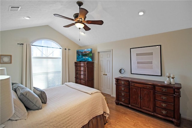 bedroom with light wood finished floors, visible vents, a ceiling fan, vaulted ceiling, and a textured ceiling