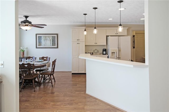 kitchen with a peninsula, white refrigerator with ice dispenser, wood finished floors, light countertops, and pendant lighting