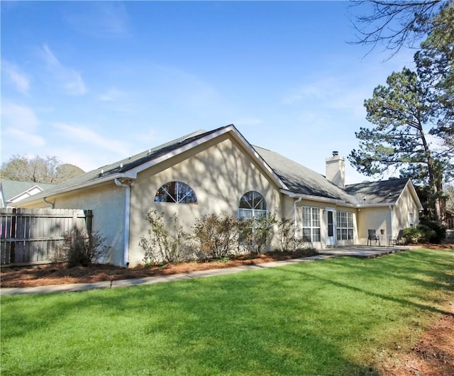 exterior space with stucco siding, a yard, a chimney, and fence