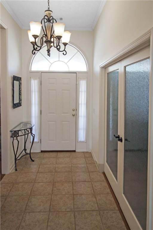entrance foyer with a notable chandelier, french doors, baseboards, and crown molding