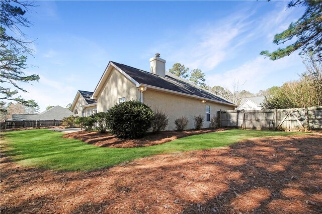 view of side of home with stucco siding, fence, a chimney, and a lawn