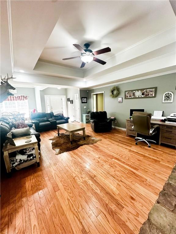 living room with ceiling fan, a tray ceiling, ornamental molding, and light hardwood / wood-style flooring