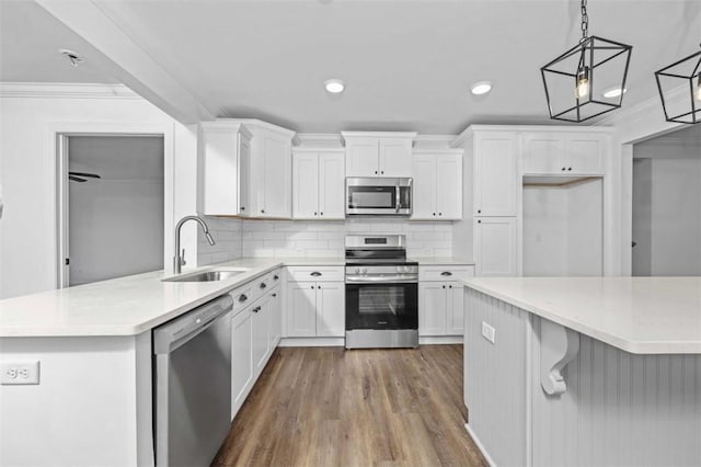 kitchen with pendant lighting, white cabinets, sink, tasteful backsplash, and stainless steel appliances