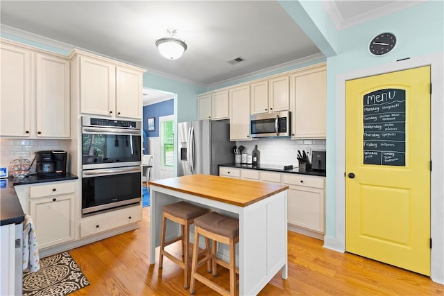 kitchen with visible vents, decorative backsplash, ornamental molding, light wood-style floors, and stainless steel appliances