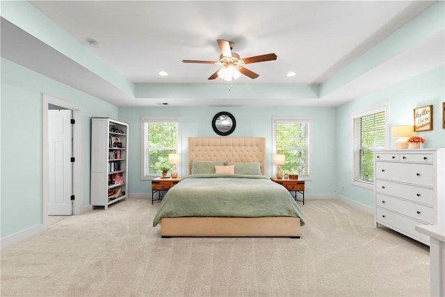 bedroom featuring baseboards, ceiling fan, a tray ceiling, and light colored carpet