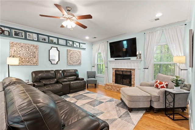 living room with a brick fireplace, ceiling fan, visible vents, and wood finished floors