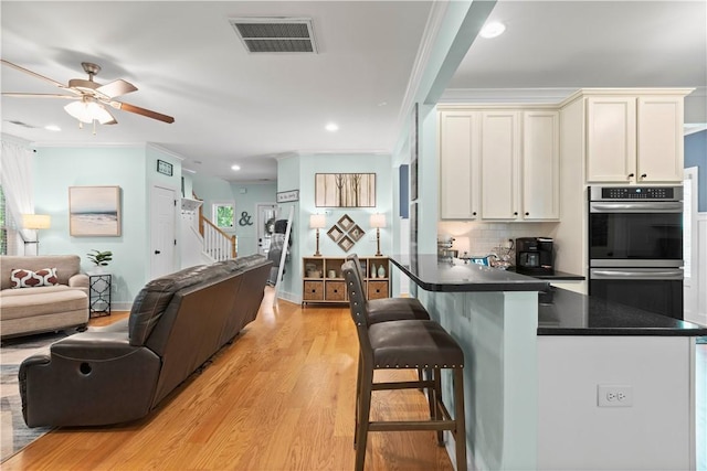 kitchen featuring visible vents, dark countertops, double oven, open floor plan, and a ceiling fan