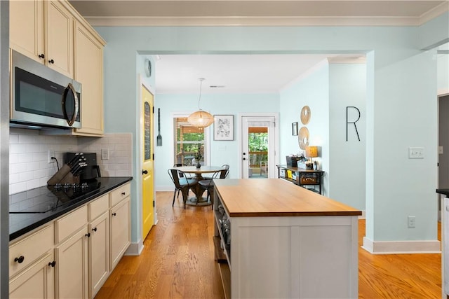 kitchen featuring cream cabinets, wood counters, stainless steel microwave, light wood-type flooring, and backsplash