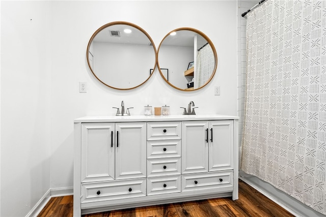 bathroom featuring double vanity, visible vents, a sink, and wood finished floors