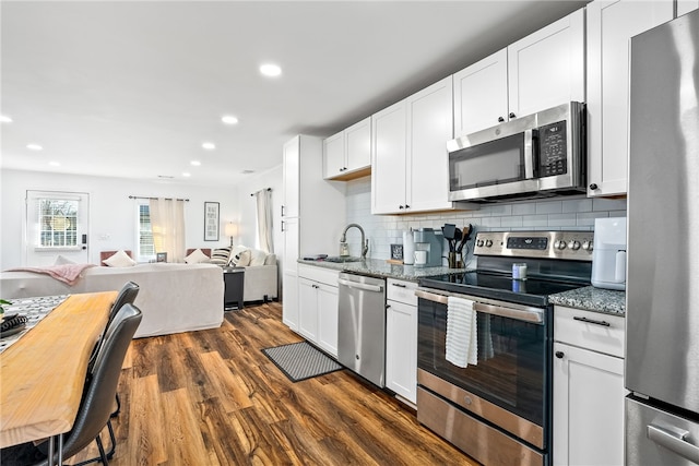 kitchen with appliances with stainless steel finishes, dark wood-style flooring, a sink, and light stone countertops