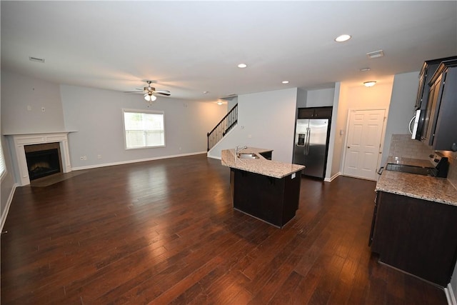 kitchen featuring ceiling fan, light stone countertops, stainless steel appliances, and an island with sink