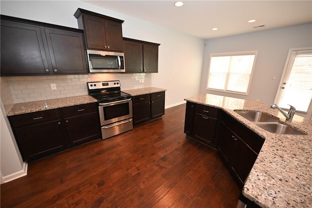 kitchen with stainless steel appliances, light stone counters, dark hardwood / wood-style floors, and sink